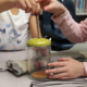 Two children holding a glass jar with a green lid and a wire wrapped straw. Only the arms and torsos of the children are visible.