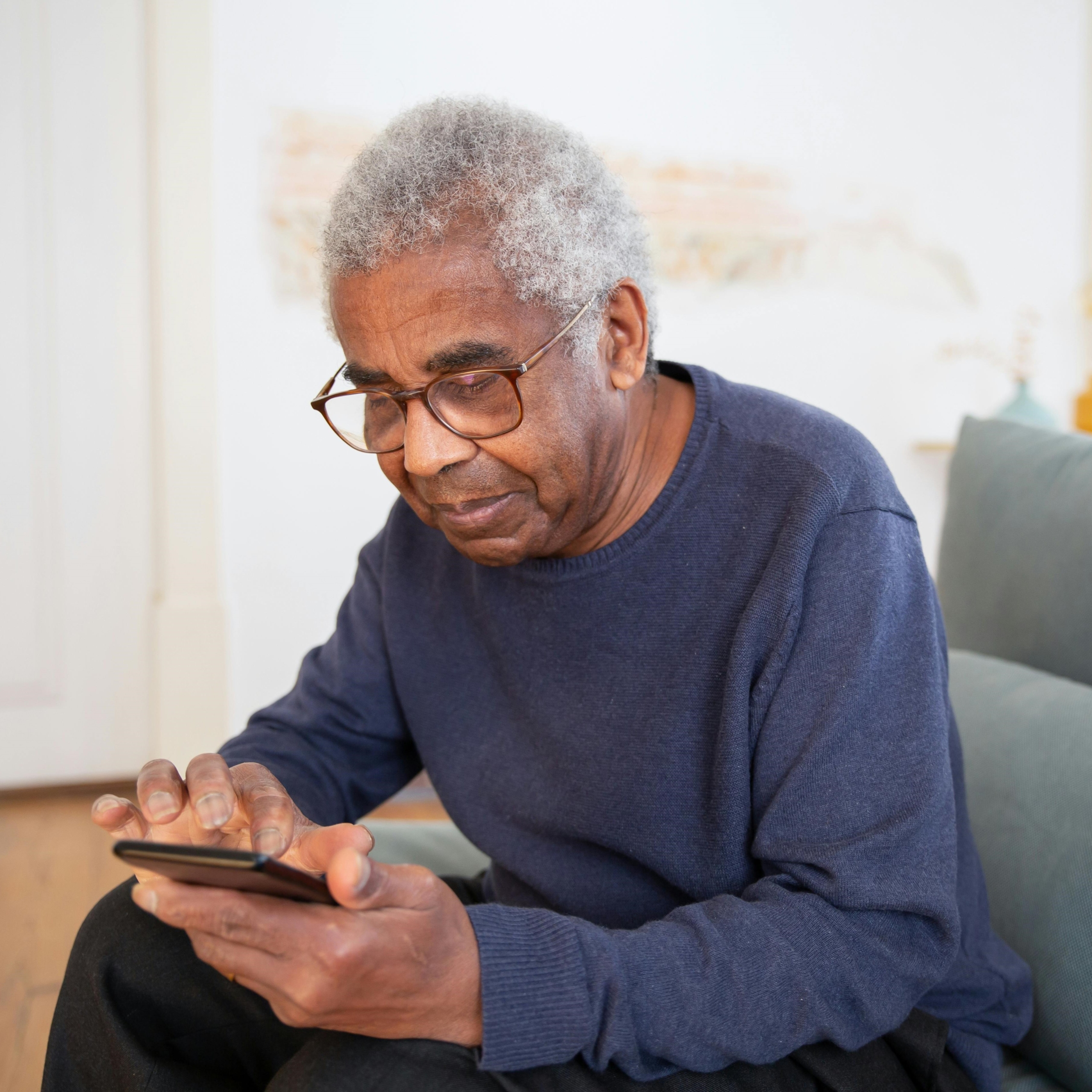 An older adult sitting on the couch while using his mobile phone.