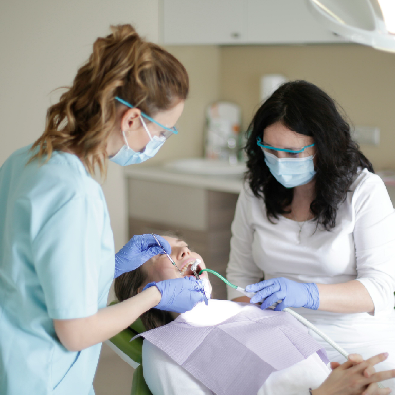 a woman lies in a dentist chair with two other women working on her teeth.