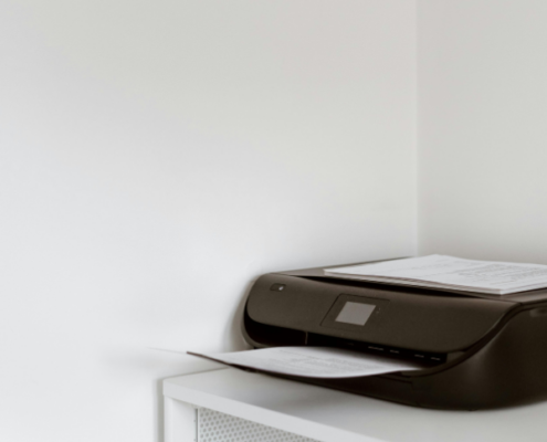 A black printer sits on top of a white shelf.