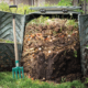 A full compost bin is opened, showing different layers of compost inside, with a green garden fork standing up beside the bin.