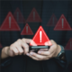 a pair of hands uses a smart phone which is overlaid with red triangle warning signs.